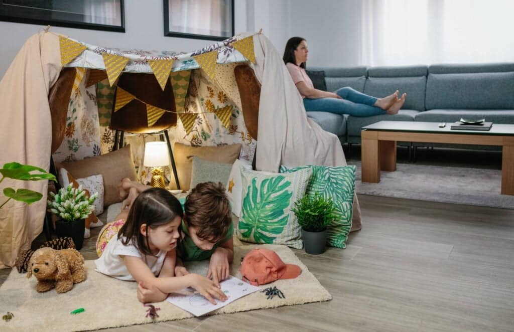Why Stay at Home Moms Should Cancel Netflix featured image - Children playing camping at home while their mother watches TV sitting on the sofa
