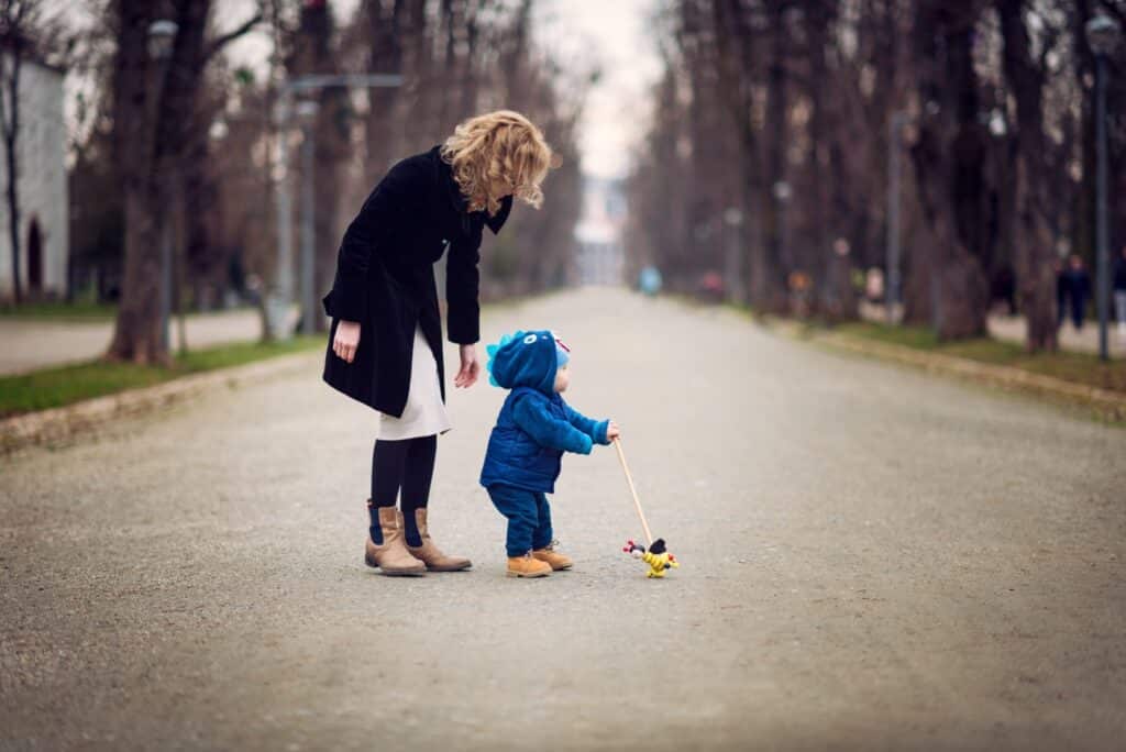 Mom standing next to a toddler who's learning how to walk. Moms sometimes feel like a bad mom even when they're with their kids.