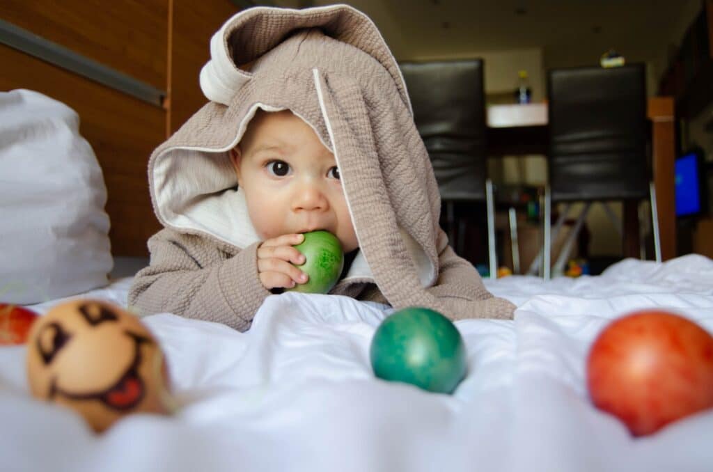 Baby Boy Easter Outfits featured image of a baby wearing a bunny costume chewing on an Easter egg