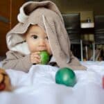 Baby Boy Easter Outfits featured image of a baby wearing a bunny costume chewing on an Easter egg