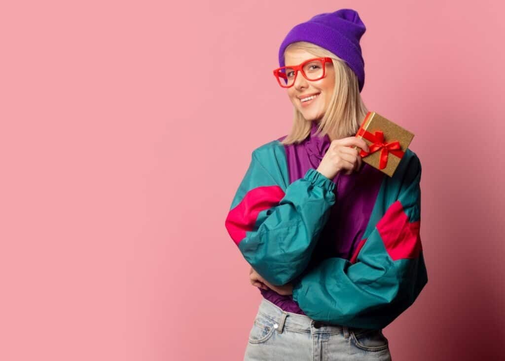 Outfit Ideas For a 90s Party featured image of a woman holding a gift and wearing 90s style windbreaker