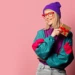 Outfit Ideas For a 90s Party featured image of a woman holding a gift and wearing 90s style windbreaker
