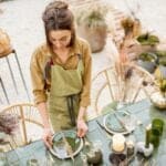 Woman decorating a boho style outdoor table surrounded by bohemian furniture and decor items