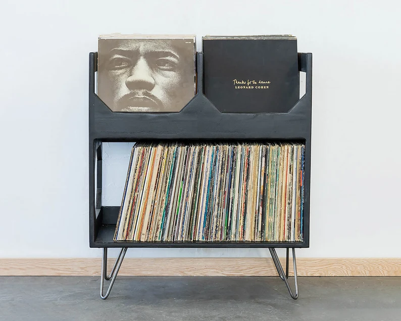 Stylish record stand in black with metal legs, it's kind of mid century modern. The bottom is a shelf for record storage and the top has too rows to forward face vinyl for display.