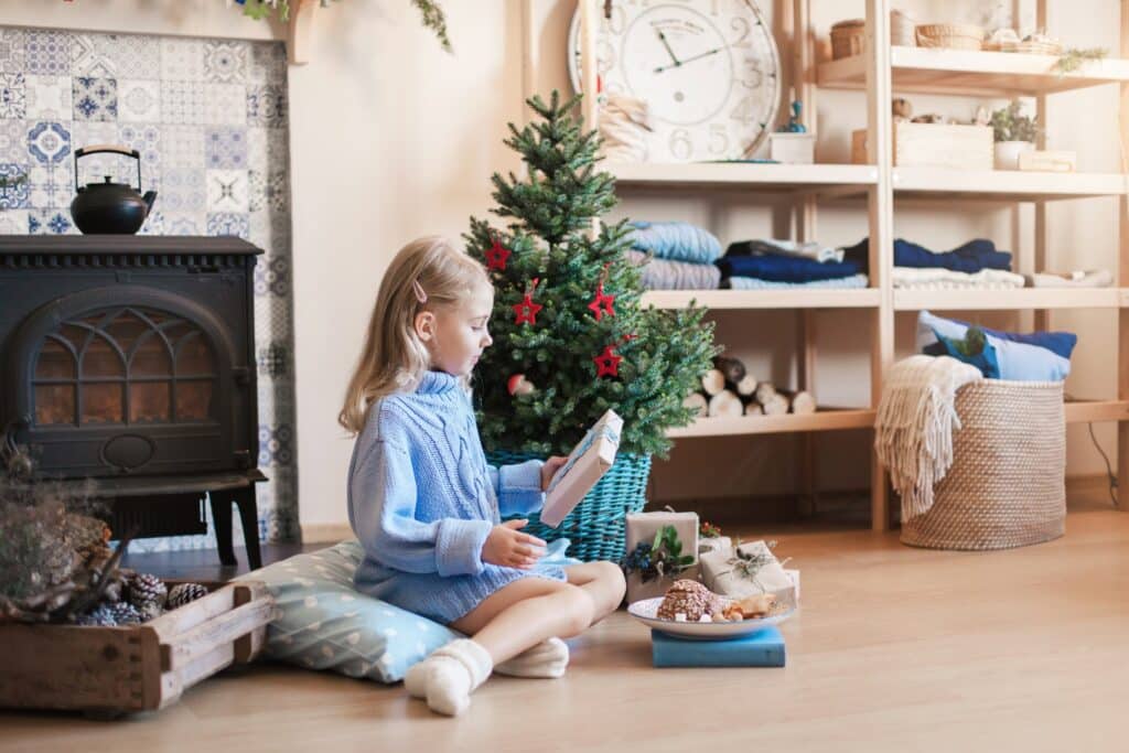 Little girl looking at a Christmas gift under a small tree - to illustrate that the 4 Christmas gift rule is a way to help kids appreciate their gifts