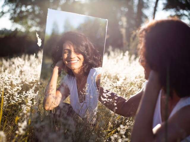 Picture of woman looking a mirror outside to illustrate that mirrors were one of the unexpected things we needed for camping