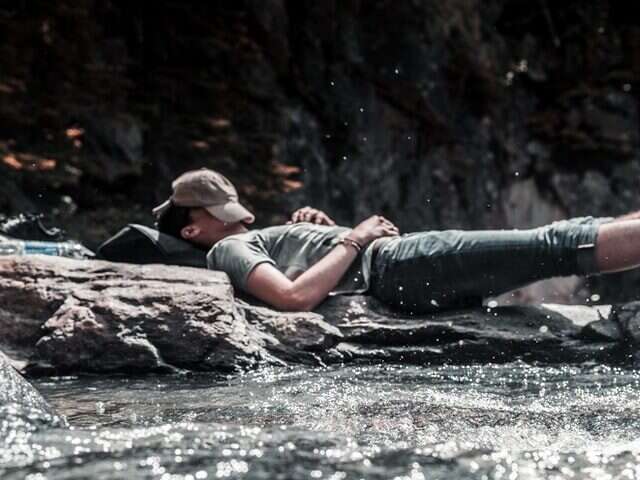 Man sleeping outside by a river with his hat over his head