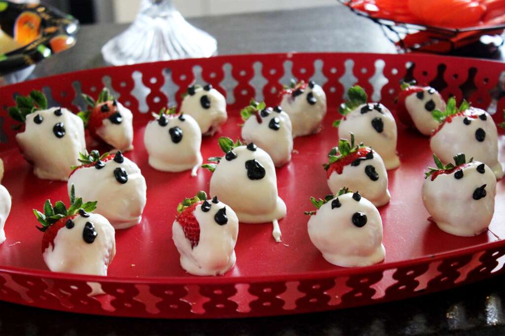 white candy melted onto strawberries made to look like ghosts on a red tray 