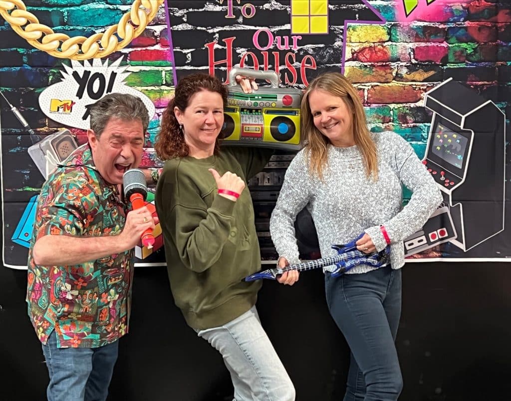Adult friends taking pictures in front of a photobooth at an 80s themed party