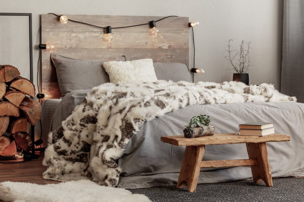 Wooden bench in the foot of the bed with grey bedding and cozy blanket