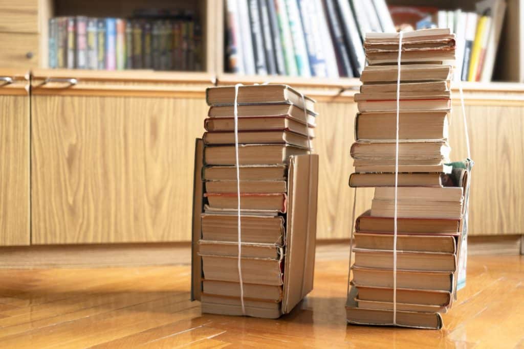 two stacks of used books tied with packthread on parquet floor in living room next to library cabinet