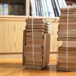 two stacks of used books tied with packthread on parquet floor in living room next to library cabinet