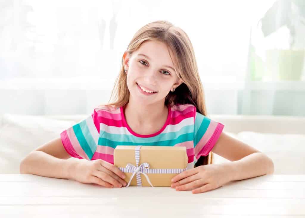 girl sitting at a table and holding small gift box.