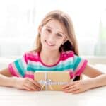 girl sitting at a table and holding small gift box.
