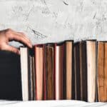 Male hand holding a book of bookshelves.